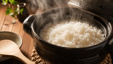 蓋を開けた土鍋から湯気が立ち、炊き上がったご飯が見えている。手前にしゃもじ